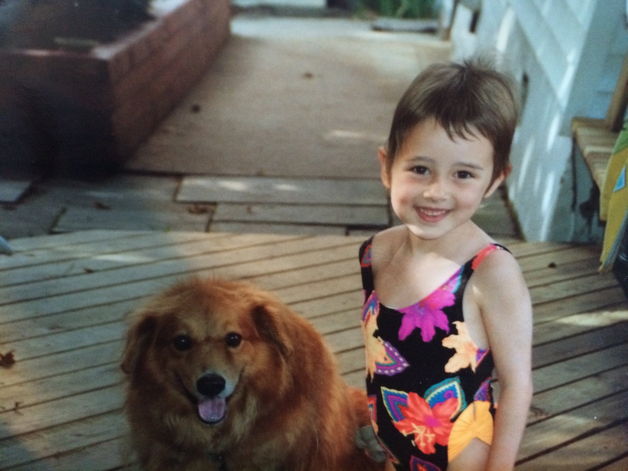 Danielle as a child with short hair growing back after treatment, smiling next to her dog