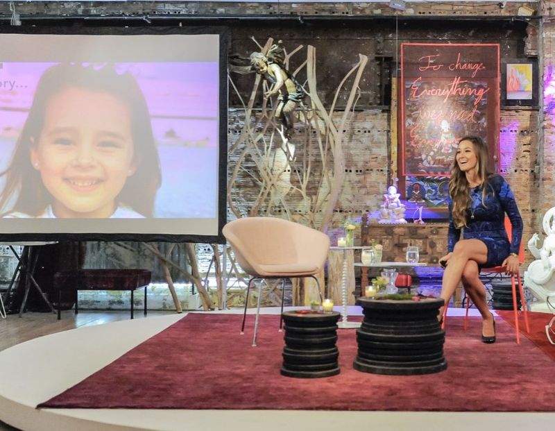 Danielle on stage beside a slide of herself as a young girl, titled My Story